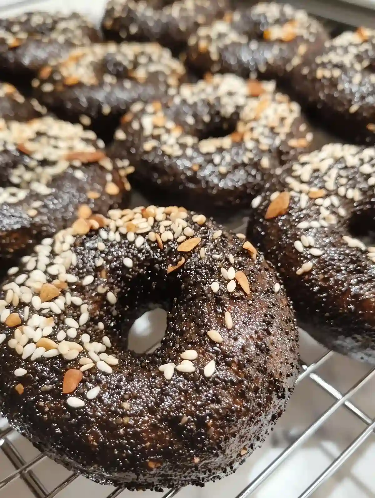 Freshly baked black Russian bagels on a wire rack, topped with sesame seeds.