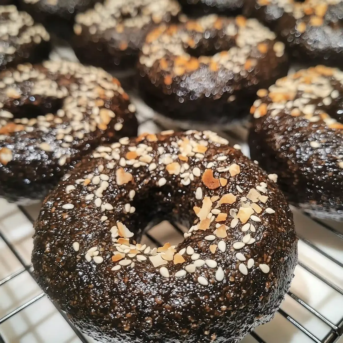 Freshly baked black Russian bagels on a wire rack, topped with sesame seeds.