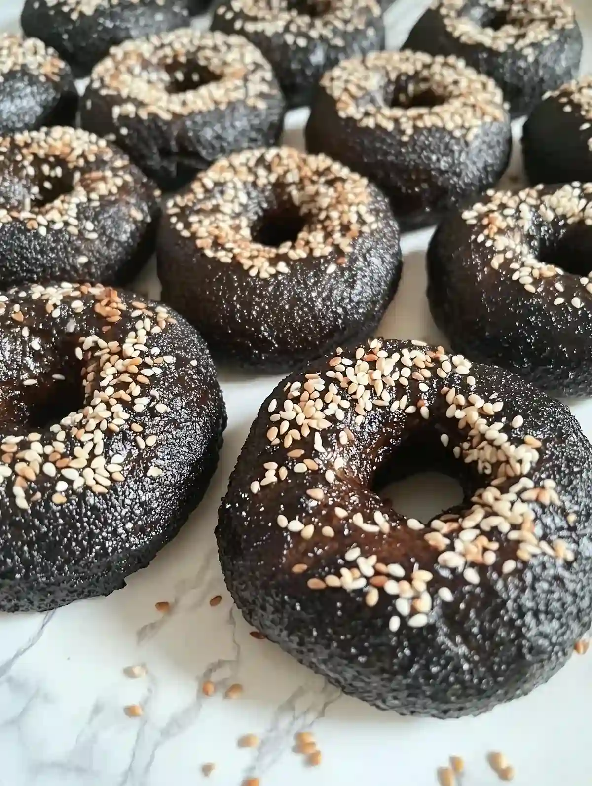 Dark cocoa bagels with sesame seeds on a marble surface