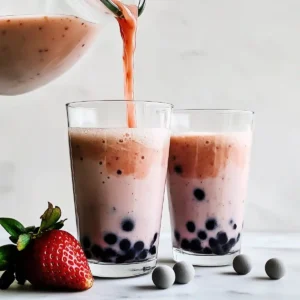 Two glasses of pink smoothie with tapioca pearls, pitcher pouring, strawberry, leaf