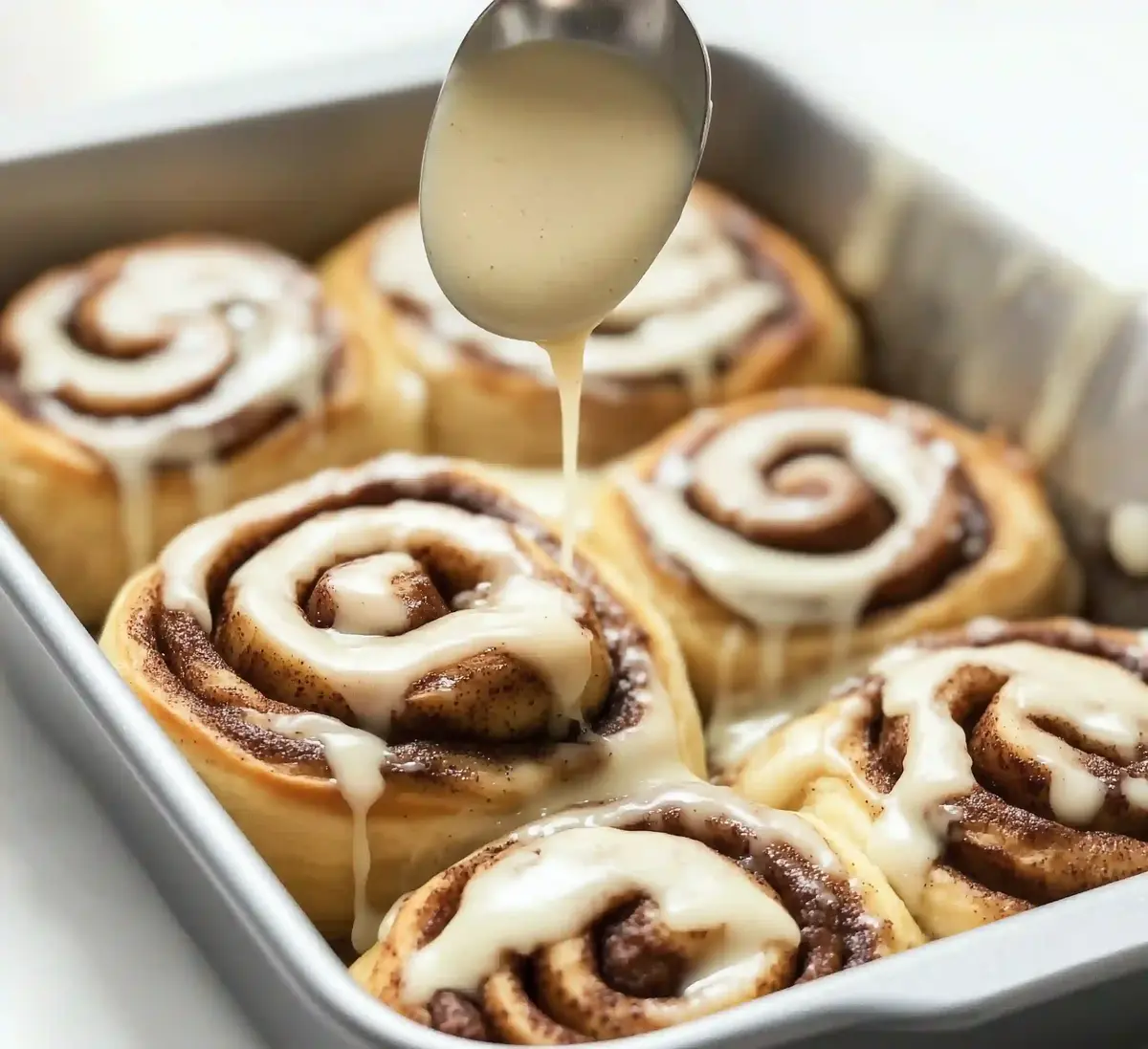 Cinnamon rolls in a baking pan, drizzled with creamy icing.