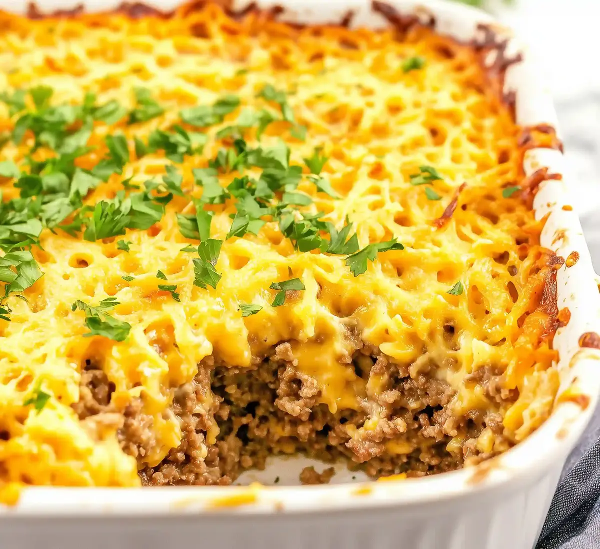 Ground beef hash brown casserole with melted cheddar, parsley garnish