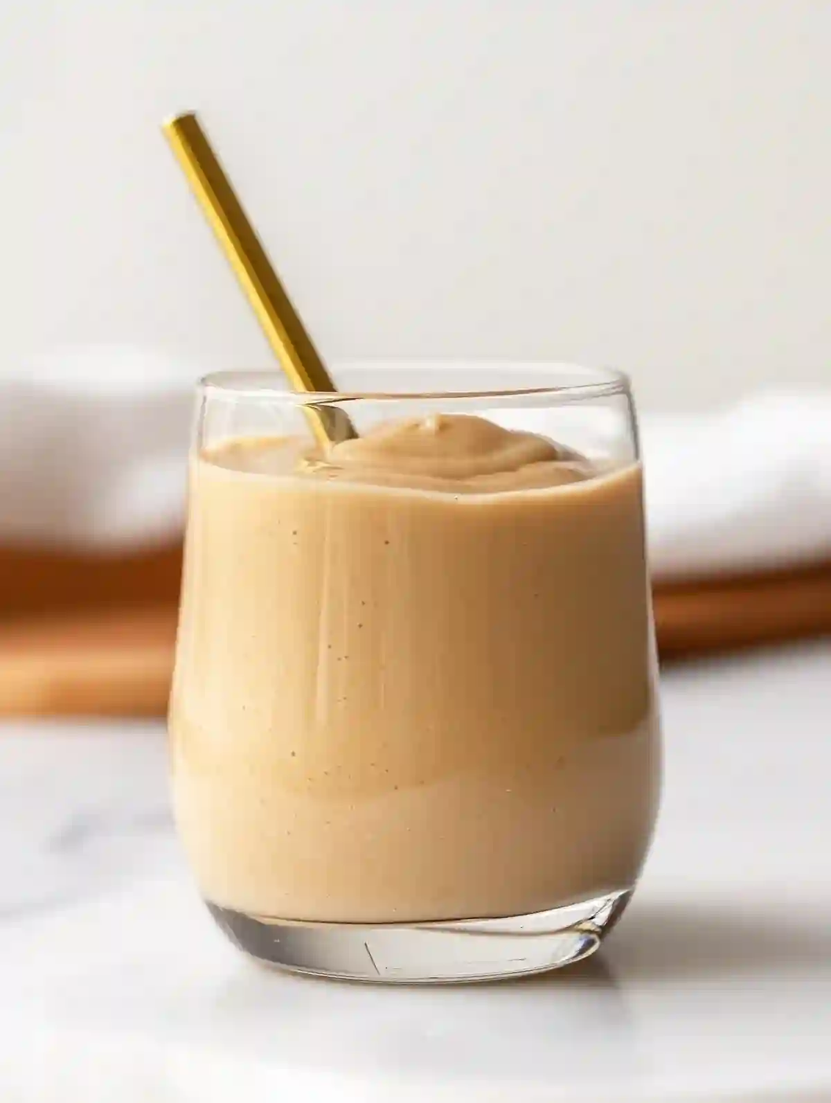 Glass of macadamia spread with a golden straw on marble surface