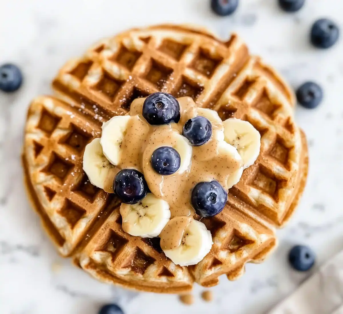 Golden-brown peanut butter waffles topped with bananas and blueberries on marble