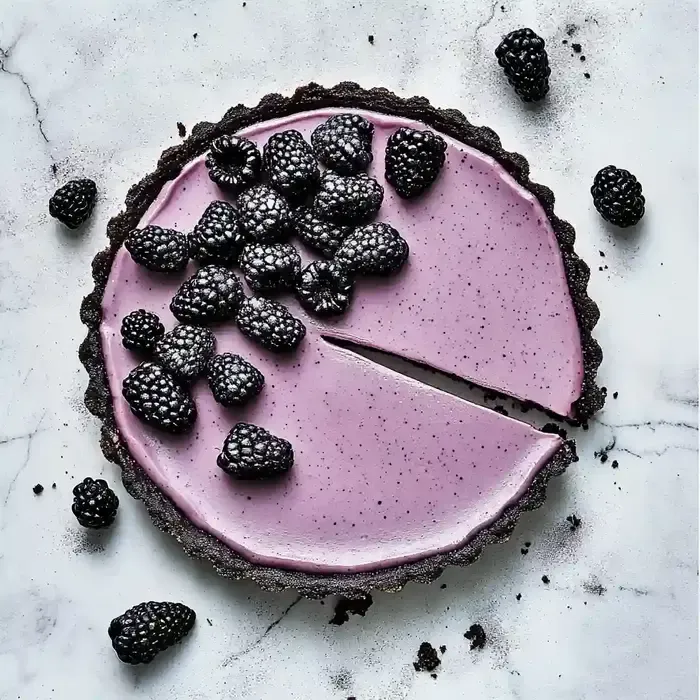 Purple tart with blackberries on a marble surface, slice removed.
