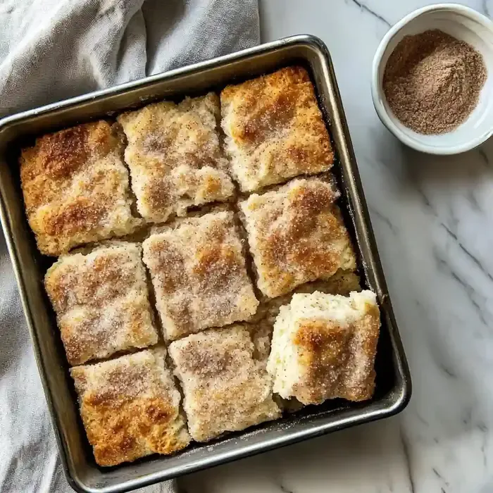 Square baking dish with cinnamon sugar biscuits on marble surface.