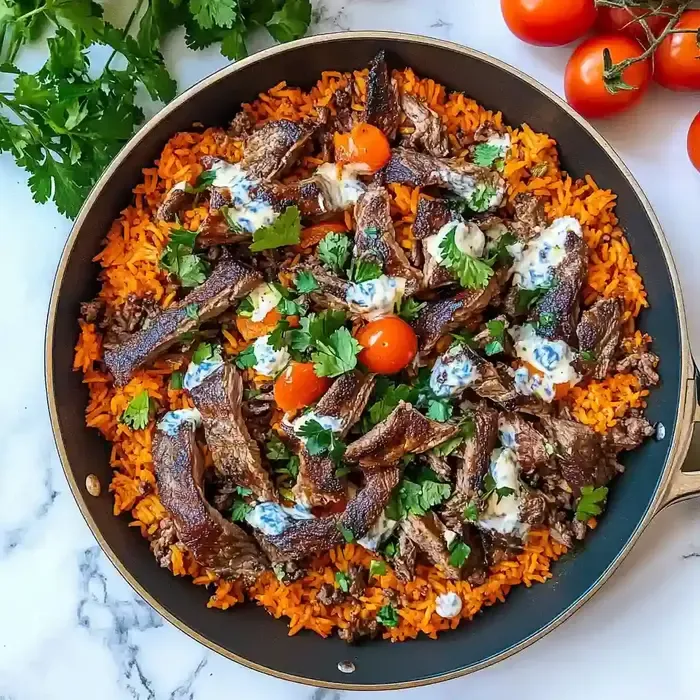 Skillet of queso rice topped with seasoned steak strips and cilantro.