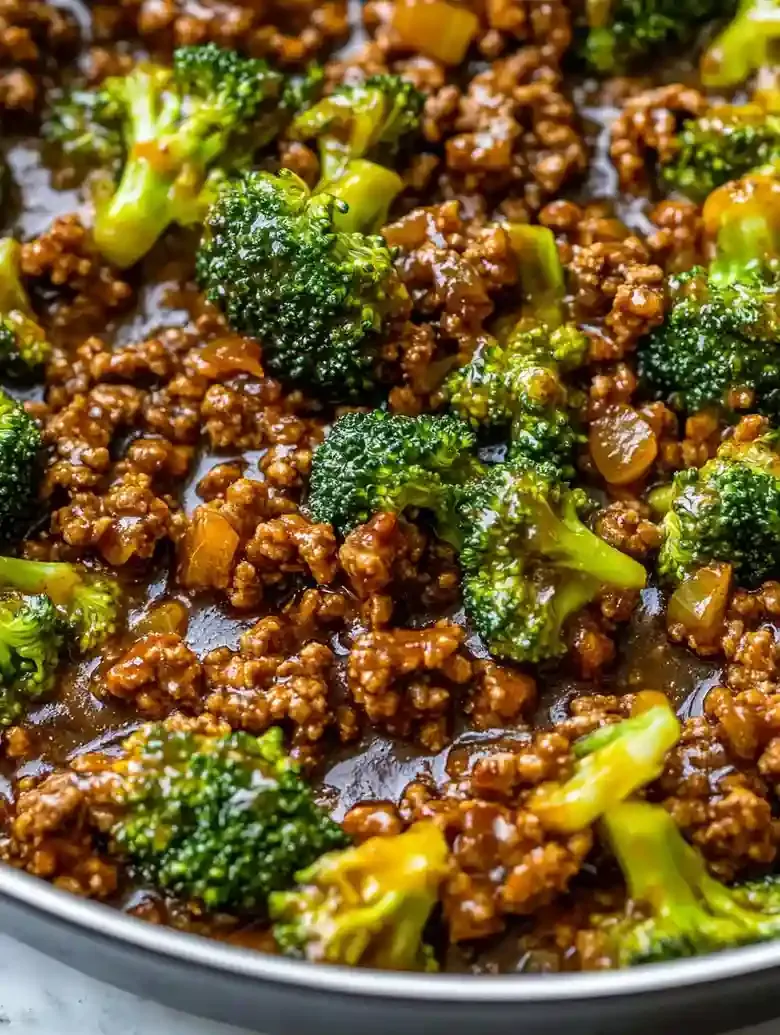 Skillet with honey garlic ground beef and broccoli on marble surface.
