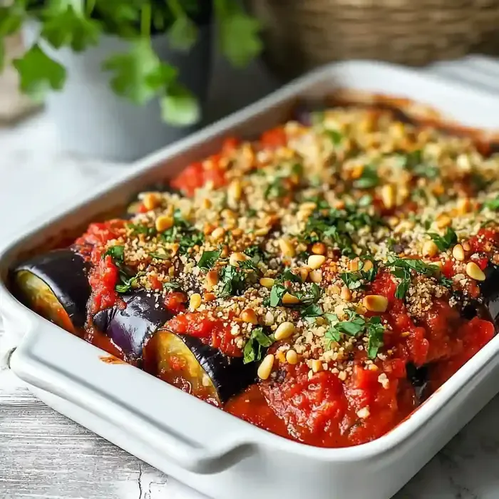 Casserole dish of eggplant rollups topped with tomato sauce and parsley.