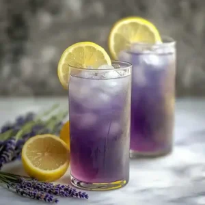 Purple cocktails with lemon slices and lavender on a marble surface.