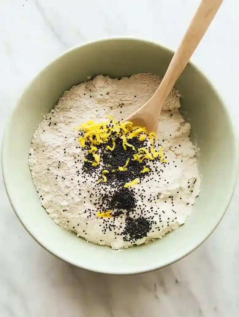 Light green mixing bowl filled with flour, poppy seeds, and lemon zest.