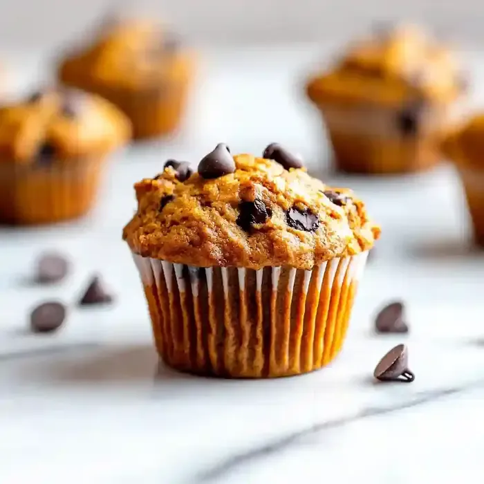 Golden-brown mini chocolate chip pumpkin muffin on white marble surface.