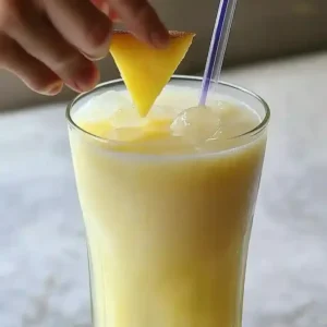 Yellow tropical drink with fruit garnish and straw on marble surface.