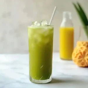 Tall glass of green matcha iced beverage with ice on marble surface.