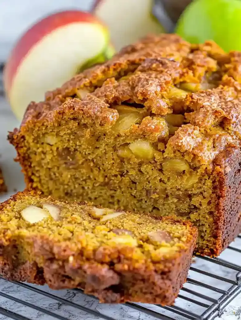 Pumpkin apple loaf on a rack, slices displayed, with a green apple beside.