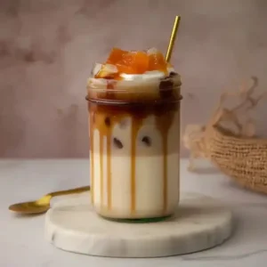 Layered drink in glass jar on marble surface with golden spoon.