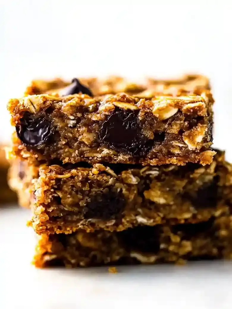 Stack of golden-brown oatmeal bars with chocolate chips on marble surface.