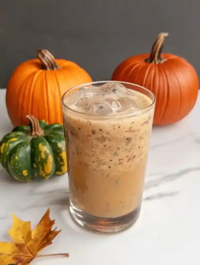 Layered cold beverage in glass beside decorative pumpkins on marble.