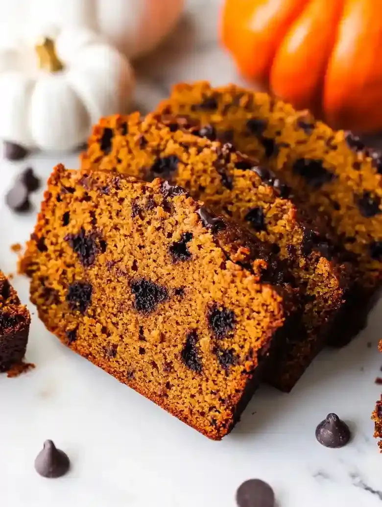 Sliced pumpkin yogurt loaf with chocolate chips on marble surface.
