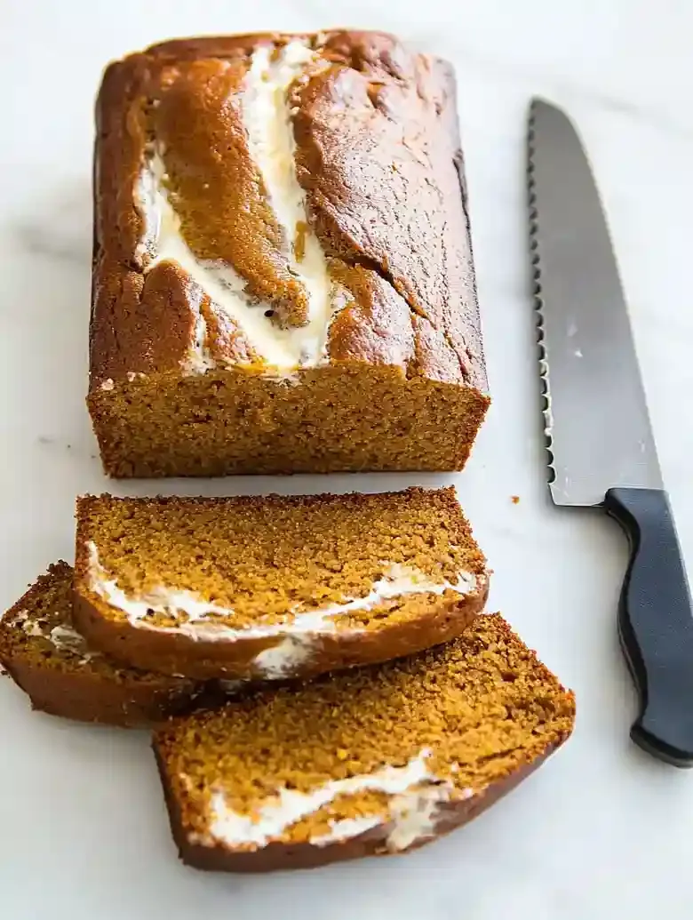 Sliced spiced pumpkin cream cheese bread on a marble surface.