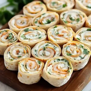 Bite-sized tortilla rollups with orange filling and green herbs on wooden platter.