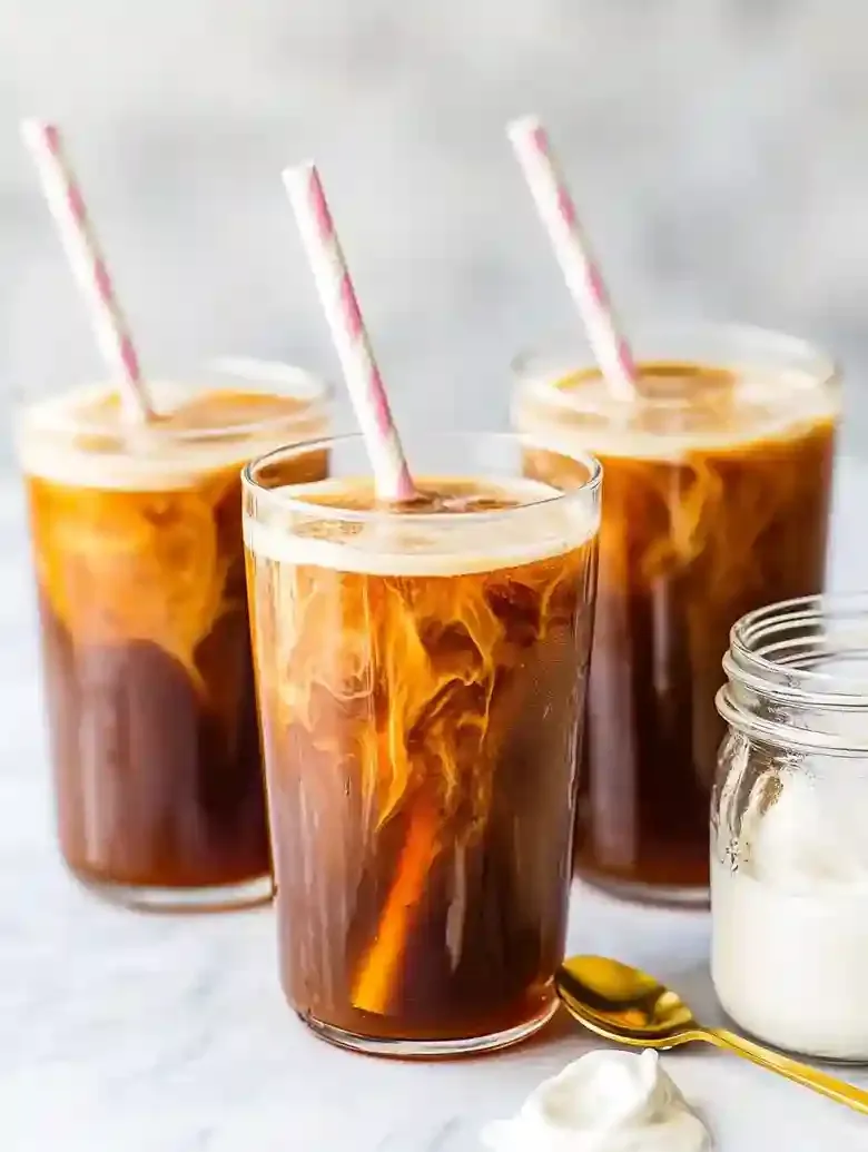 Four tall glasses of cold brew coffee with sweet cream and striped straws.