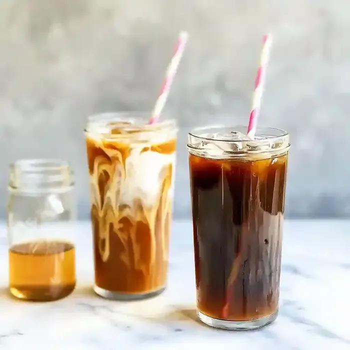 Two tall glasses of cold brew coffee with ice and cream, on marble surface.