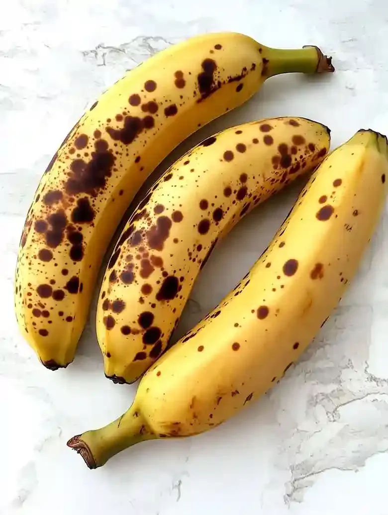 Three ripe, speckled bananas on a white marble surface.