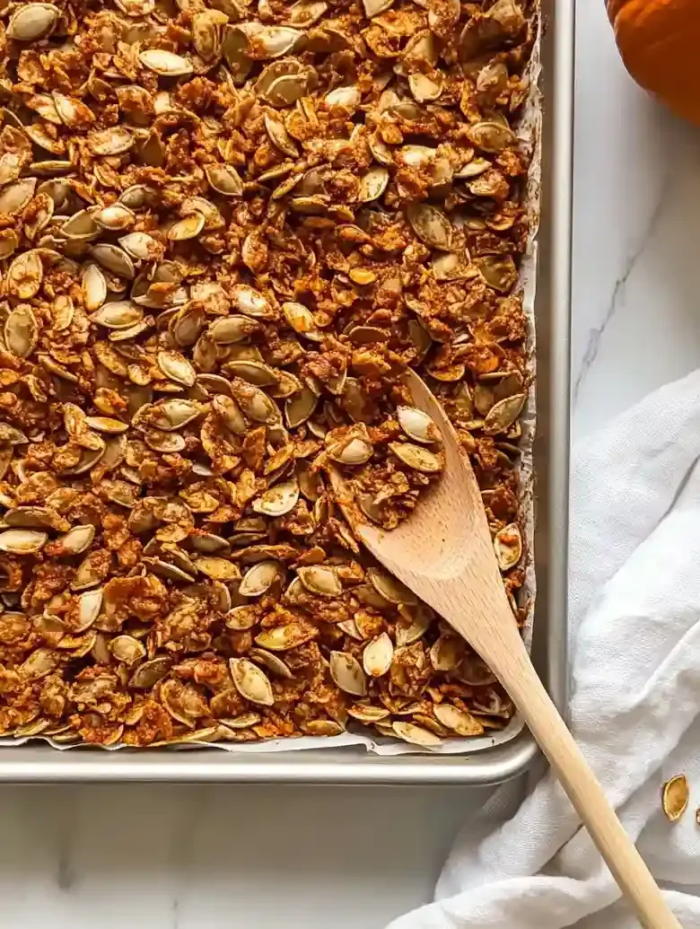 Baking sheet of crispy chili-roasted pumpkin seeds with a wooden spoon.