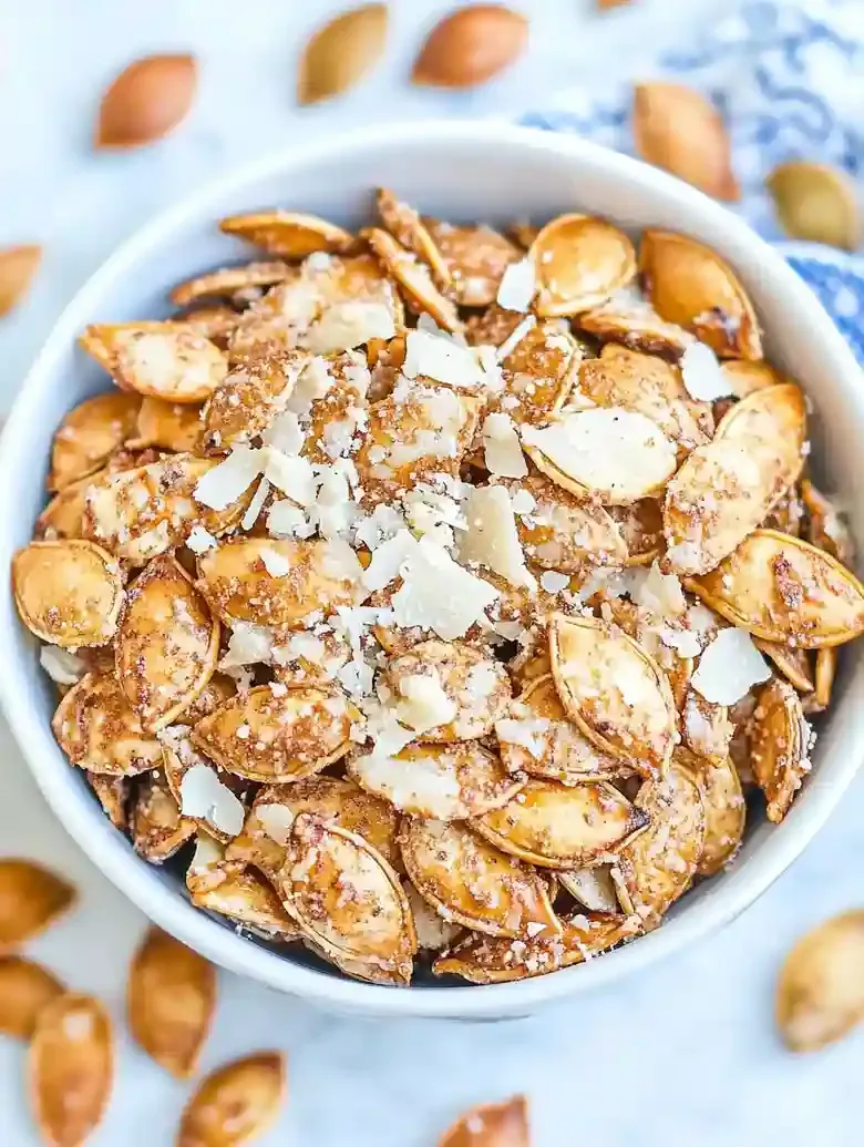 Bowl of garlic Parmesan pumpkin seeds on a white marble surface.