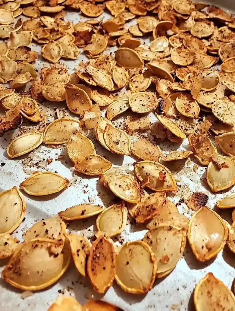 Roasted pumpkin seeds on a marble baking sheet, golden brown with seasoning.