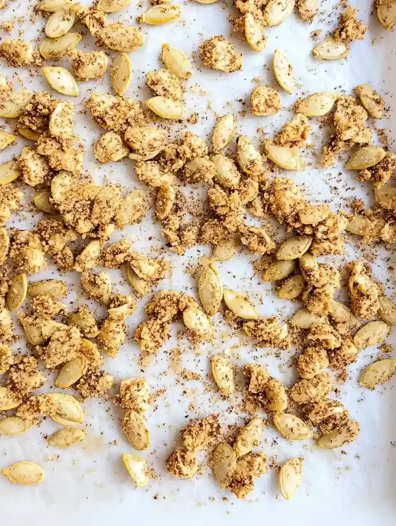 Roasted pumpkin seeds with seasoning on white marble surface.