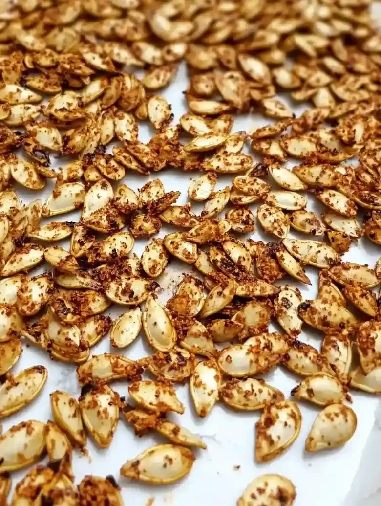 Closeup of seasoned roasted pumpkin seeds on a white marble surface.