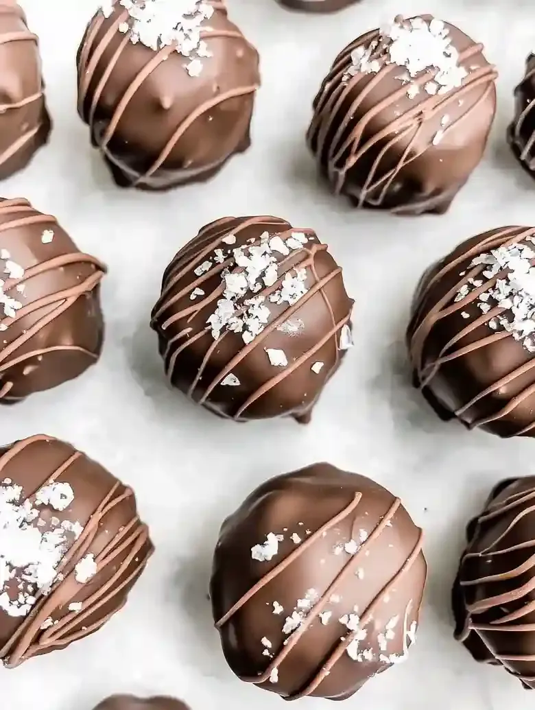 Chocolate-covered spheres on marble, drizzled and sprinkled with sea salt.
